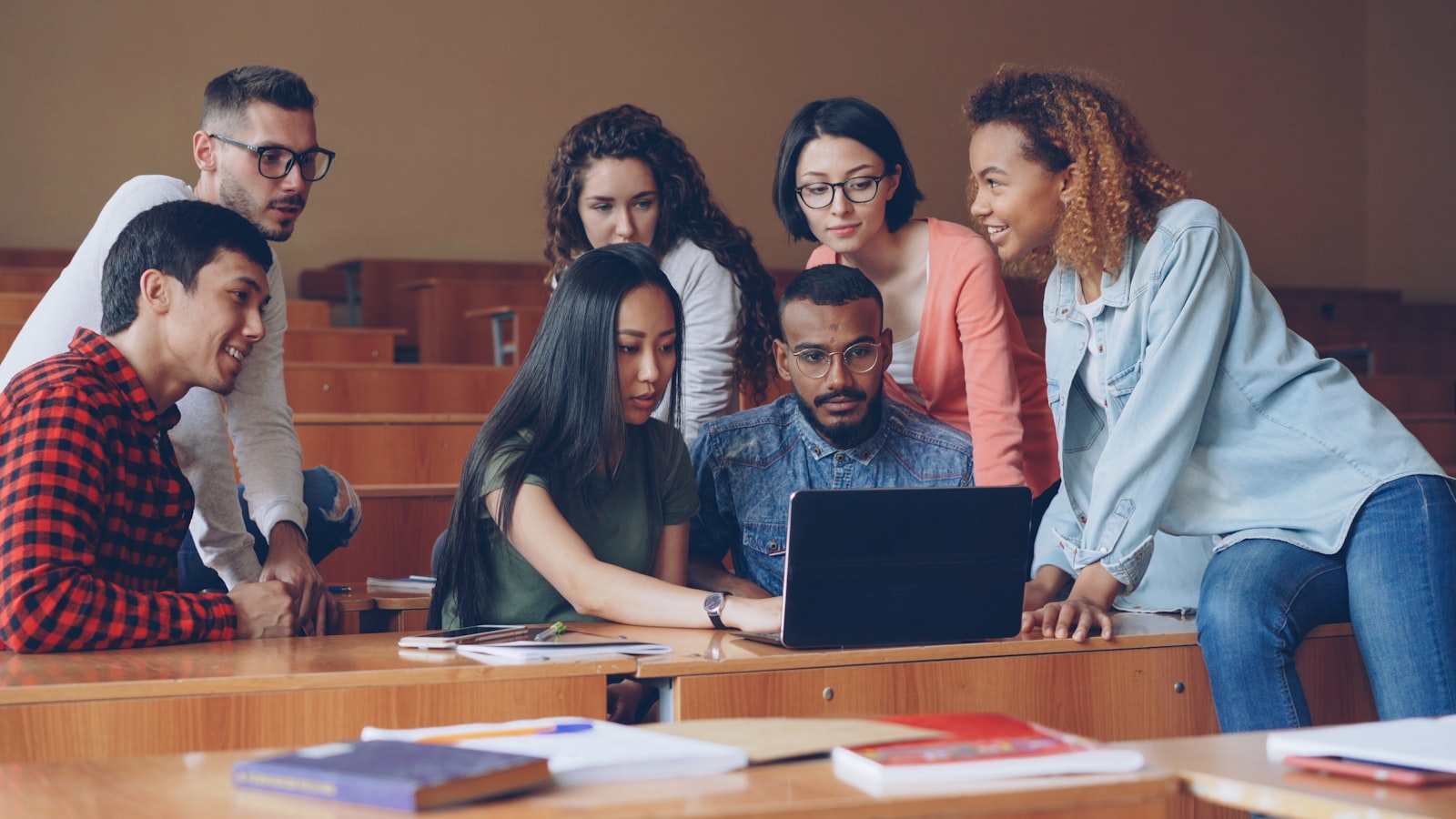 Grupo de jovens estudantes de diferentes origens estudando juntos em volta de um laptop